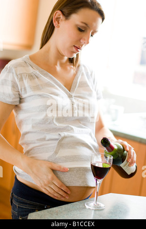 Worried looking pregnant woman drinking wine Stock Photo