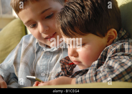 Ten year old boy shows his two year old cousin how to operate a new Video Ipod Stock Photo