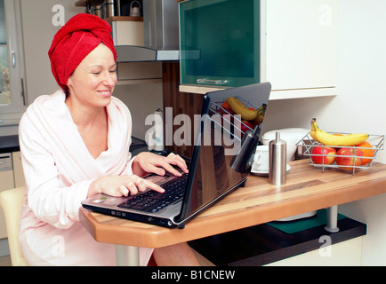 woman in bath robe using laptop in kitchen Stock Photo