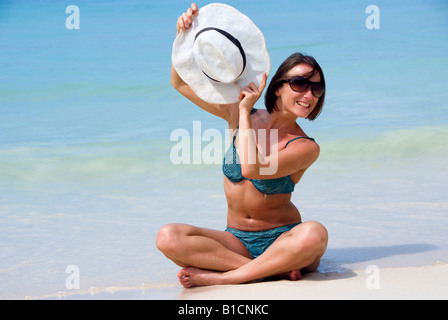 young woman in bikini and with sunglasses at the beach, holding her hat Stock Photo