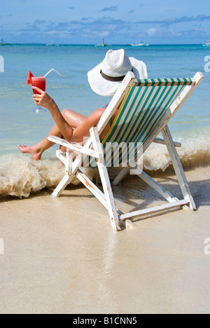 woman with cocktail sits in a folding chair at the beach, enjoying holidays, Philippines Stock Photo