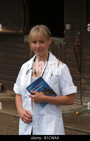 Female vet standing in a stable yard wearing a white coat and stethoscope holding a Pet Passport Stock Photo