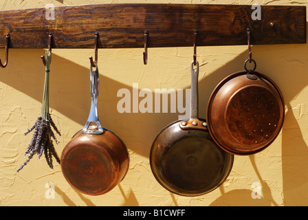 Vintage copper pots and pans hanging from a wooden wine barrel rack on a stucco wall Stock Photo