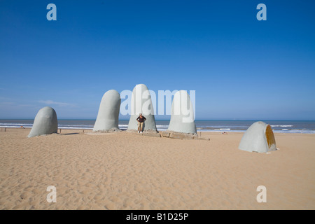 Tourist posing in the hand of a drowning man sculpture in Playa Brava beach Punta del Este Uruguay Stock Photo