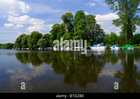 View of the River Thames in Pangbourne West Berkshire England UK with trees reflected in water and small boats moored on bank Stock Photo