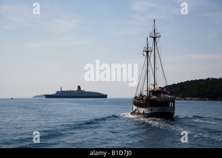 The sailing ship Astral leaving Dubrovnik towards Island of Lopud with Cunard QE2 at anchor Stock Photo