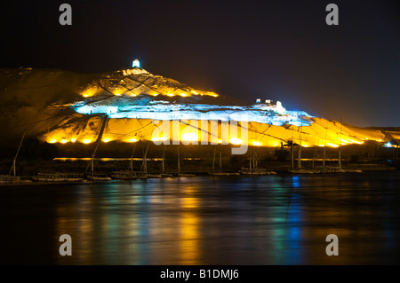 Lights illuminate the Tombs of the Nobles at dusk across the Nile River from Aswan Egypt Stock Photo