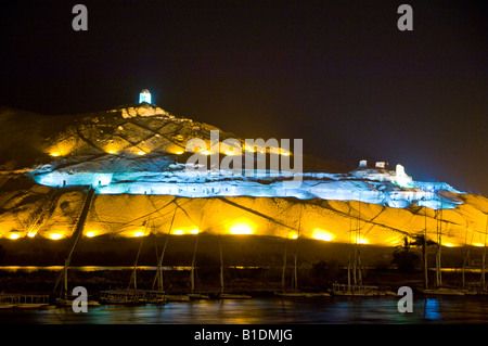 Lights illuminate the Tombs of the Nobles at dusk across the Nile River from Aswan Egypt Stock Photo