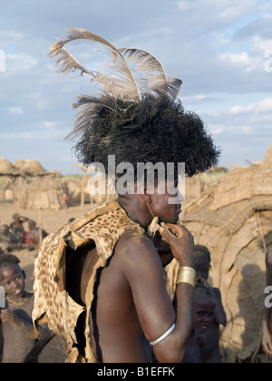 In the early morning, a Dassanech man puts on his serval cat skin cape and ostrich-feather headdress to participate. Stock Photo