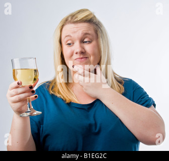 overweight blonde young woman drinking white wine looking worried and concerned about her alcohol intake Stock Photo