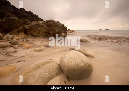 Waves rushing around large boulders on the shoreline of Porth Nanven beach St Just Cornwall UK Stock Photo