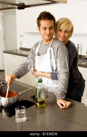 Young man cooking food and a young woman embracing him from behind in the kitchen Stock Photo