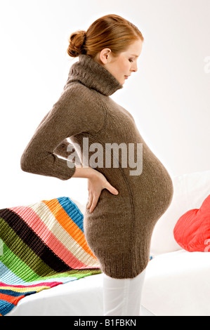 Side profile of a pregnant young woman standing and looking at her abdomen Stock Photo