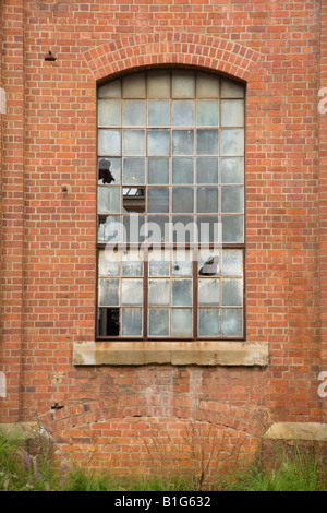 old arch style window frame in red brick wall with broken glass panes Stock Photo