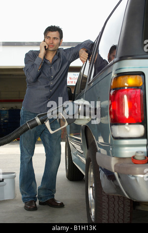 Man using cell phone leaning on van with fuel pump Stock Photo