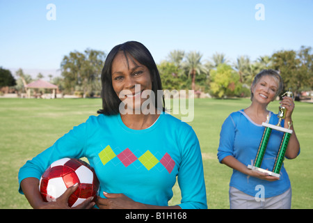 Senior women holding soccer ball and trophy in park, portrait Stock Photo