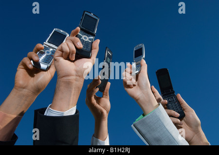 Business people holding mobile phones up in air, close-up of hands Stock Photo