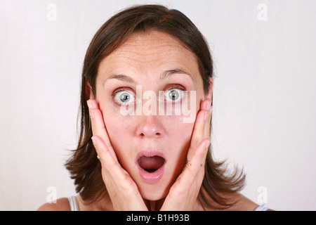 Young brunette open mouthed brunette woman holds head in hands looking shocked stunned amazed aghast surprised Stock Photo