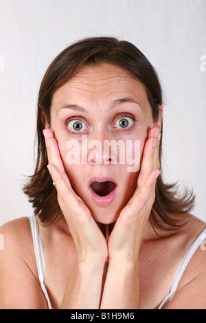 Young brunette open mouthed brunette woman holds head in hands looking shocked stunned amazed aghast surprised Stock Photo