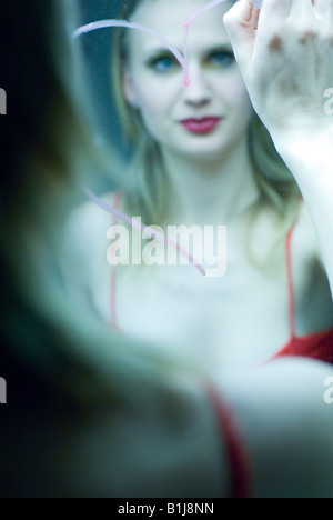 young blond woman drawing a heart onto a mirror with lipstick Stock Photo
