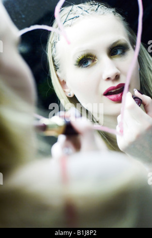 young blond woman putting on lipstick in front of a mirror. A heart is painted with lipstick on the mirror Stock Photo