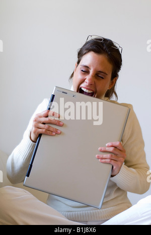 young woman biting on her laptop in frustration Stock Photo