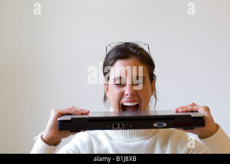 young woman biting on her laptop in frustration Stock Photo