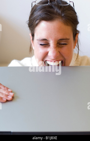 young woman biting on her laptop in frustration Stock Photo