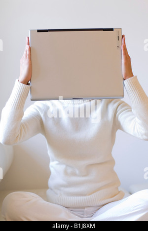 young woman sitting cross-legged, holding her notebook in front of her face Stock Photo