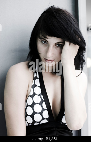 young serious woman wearing a black and white dress, with her hand in her hair Stock Photo