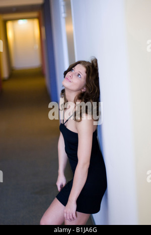 young, beautiful brownhaired woman in a black dress, leaning at a wall, exhausted and nerved Stock Photo