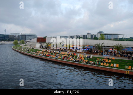 people on canvas chairs at the Spree bank in front of the memorial place Berlin Wall and the Parliament, Germany Stock Photo