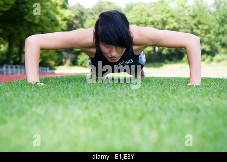 young woman with sport dress doing push-ups on a lawn Stock Photo