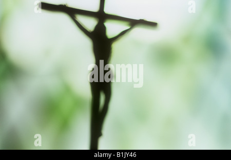 Impressionistic Jesus Christ hanging from crucifix silhouetted against green and white diamond leaded window Stock Photo