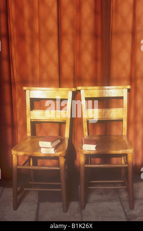 Two simple wooden chairs with three red books backed against red curtain with window shadows in warm light Stock Photo