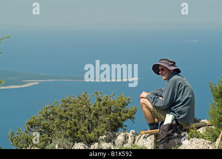 bearded middle aged man hiking through stony landscape having a pause on the top of the mountain Televrina Stock Photo