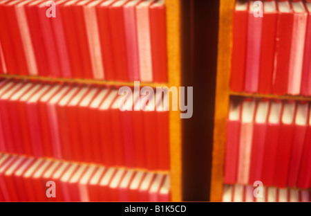 Impressionistic rows of near-identical red text or hymn or prayer books in two bookcases in warm light Stock Photo