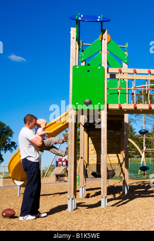 Father helping his toddler son climb up the equipment in an adventure playground. Stock Photo