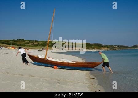A couple pull their boat up the sand on middle town beach st martin's isles of scilly Stock Photo