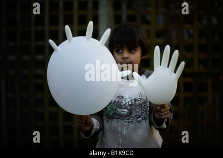 Six year old boy holding inflated latex rubber glove outside in garden He is mixed race indian english with olive skin Stock Photo