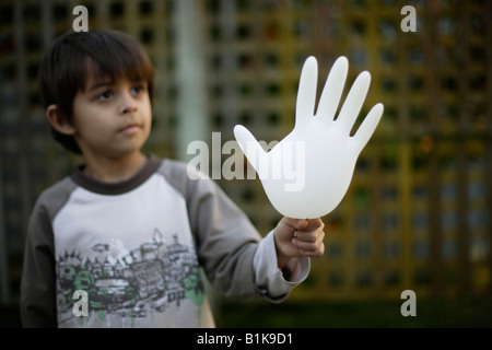 Six year old boy holding inflated latex rubber glove outside in garden He is mixed race indian english with olive skin Stock Photo