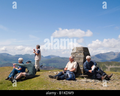 Group of Welsh Ramblers sitting by a summit cairn trig point on Moelwyn Mawr in Snowdonia National Park in summer North Wales UK Stock Photo