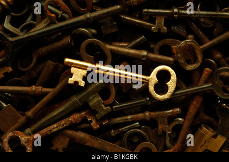 A shiny glowing new gold or brass skeleton key among a pile of old rusted antique keys Stock Photo
