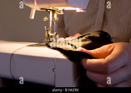 Close up of a woman using a sewing machine to stitch black fabric. Stock Photo