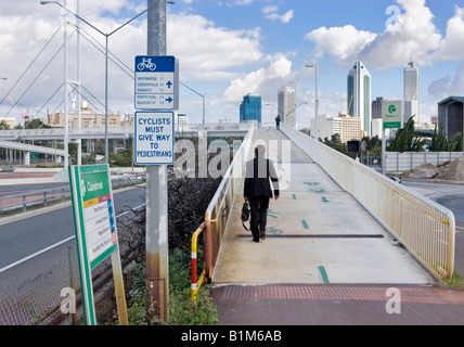 A suited man with a briefcase walking up an overpass with skyscrapers in the distance. Perth, Western Australia Stock Photo