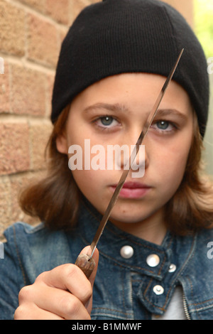 Young teenager girl with sharp knife denim jacket and black beany hat in urban street alley with brick wall POSED BY MODEL Stock Photo