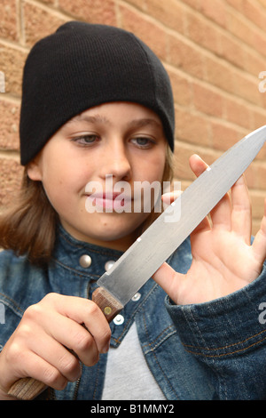 Young teenager girl with sharp knife denim jacket plotting plan revenge in urban street alley with brick wall POSED BY MODEL Stock Photo