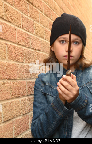 Young teenager girl with sharp knife denim jacket and black beany hat in urban street alley with brick wall POSED BY MODEL Stock Photo