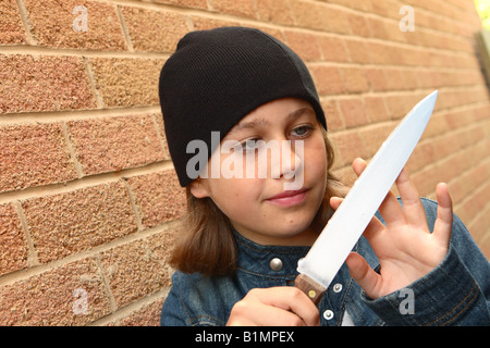 Young teenager girl with sharp knife denim jacket plotting plan revenge in urban street alley with brick wall POSED BY MODEL Stock Photo