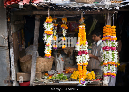 INDIA MUMBAI MAHARASHTRA Young Indian boy making and selling brightly colored garlands of flowers in a small shop Stock Photo